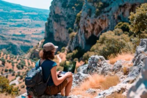 Tourist sitting on a rocky cliff in the mountains using a laptop