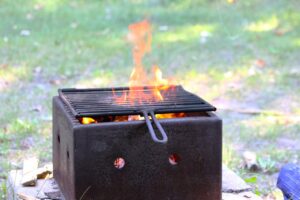 Portable barbecue grill with flames and glowing coals on grass and dirt ground