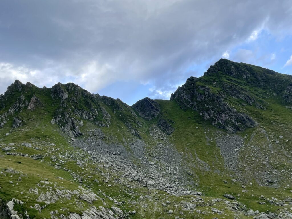 Alpine meadow with rocky peaks and green slopes under partly cloudy sky