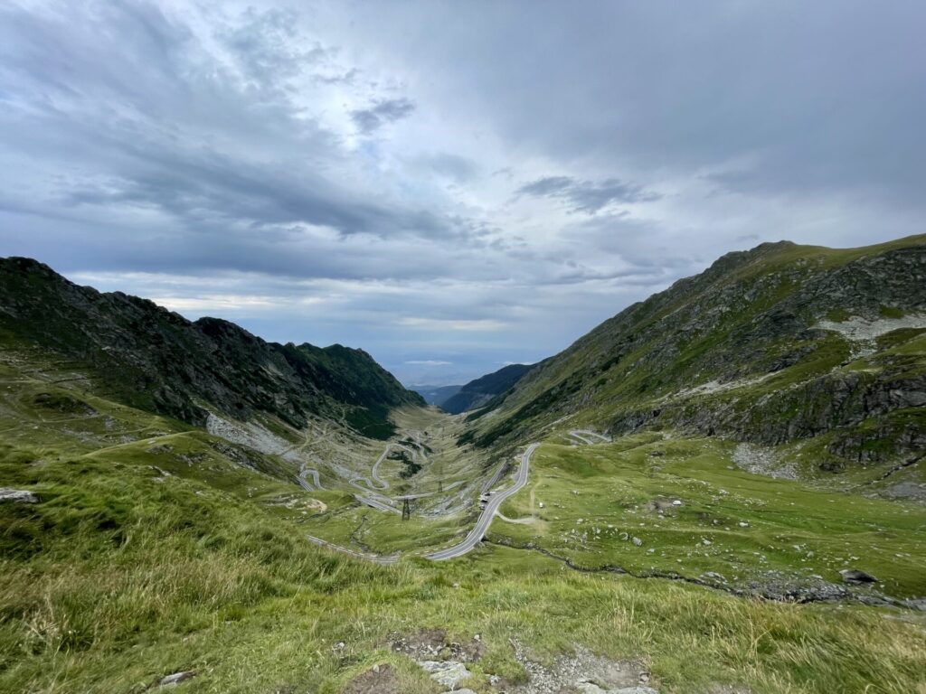 Winding mountain road through a lush green valley with steep rocky slopes under a cloudy sky