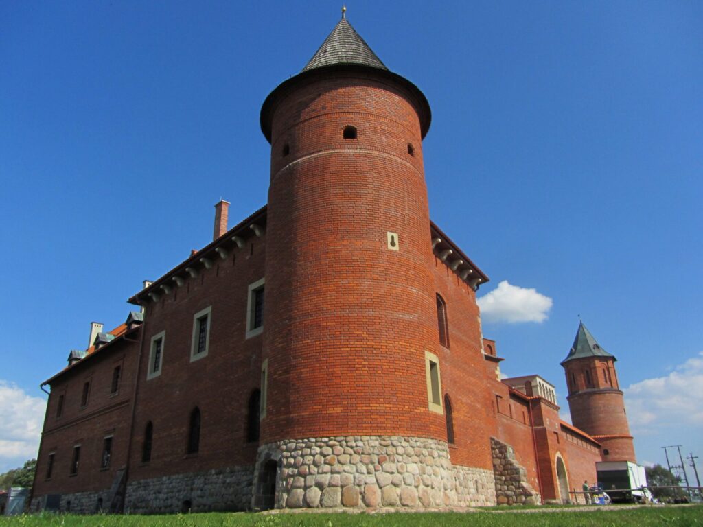 Red brick castle with conical tower and stone foundation under clear blue sky