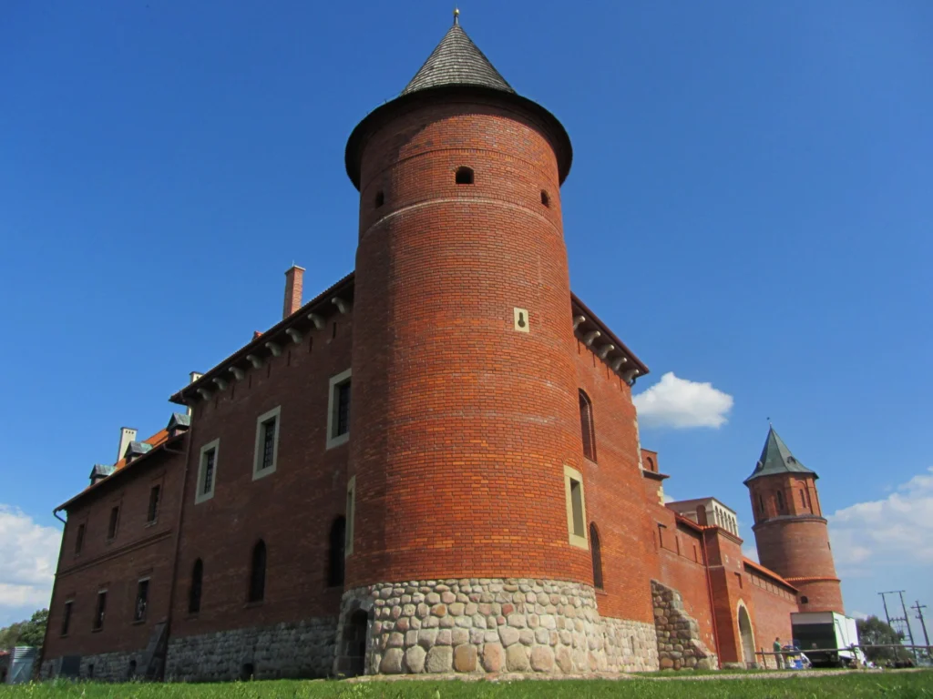Red brick castle with conical tower and stone foundation under clear blue sky