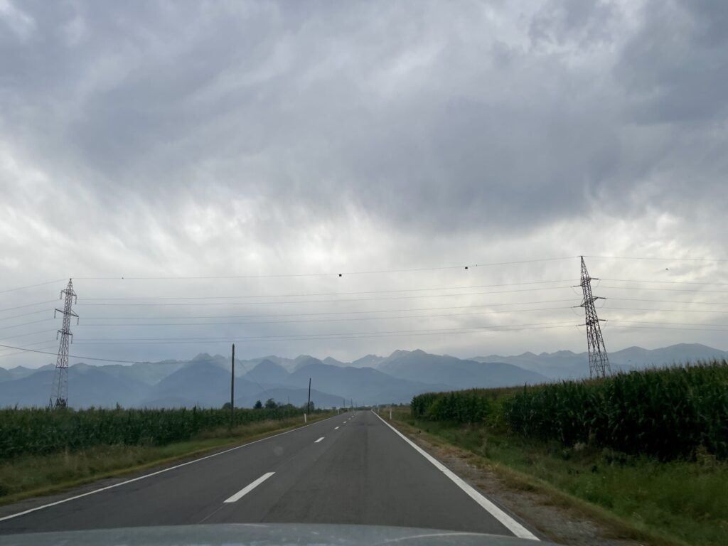 Straight road stretching toward distant mountains under overcast sky, with electrical transmission towers and crop fields on either side