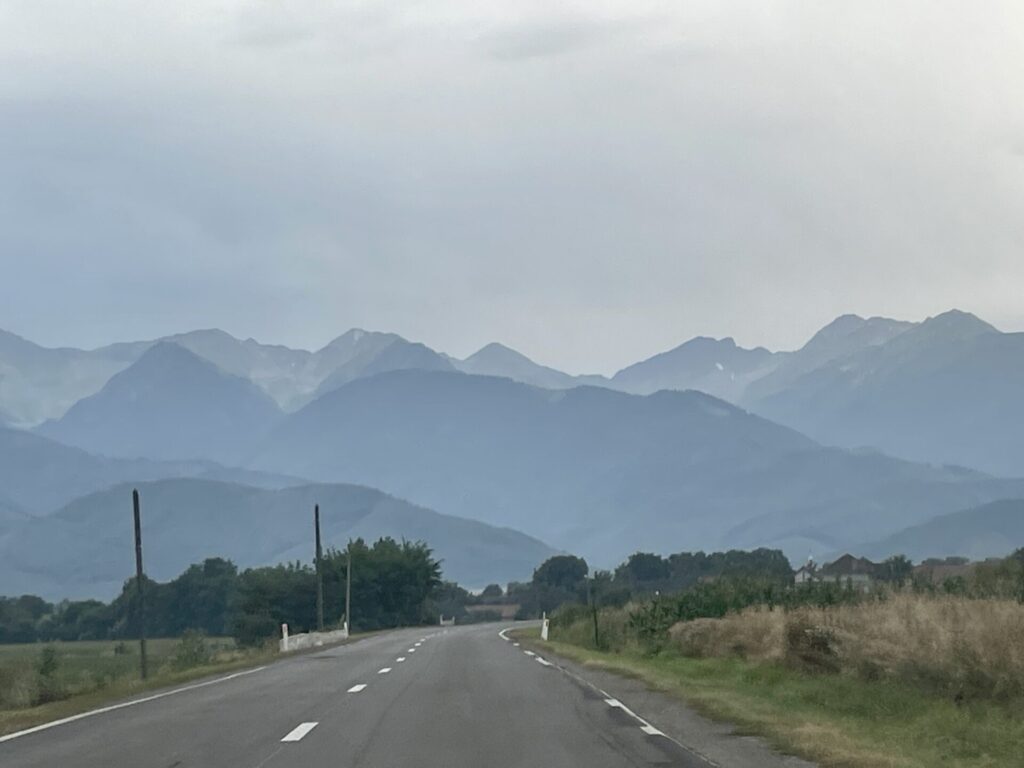 Straight road stretching toward distant mountains shrouded in mist, with vegetation and utility poles lining both sides