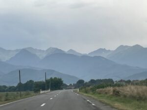 Straight road stretching toward distant mountains shrouded in mist, with vegetation and utility poles lining both sides