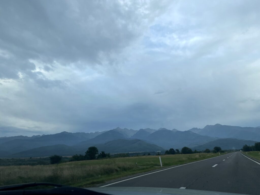 Straight highway stretching toward distant mountains under a cloudy sky, with green fields on either side