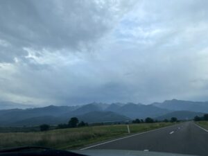 Straight highway stretching toward distant mountains under a cloudy sky, with green fields on either side