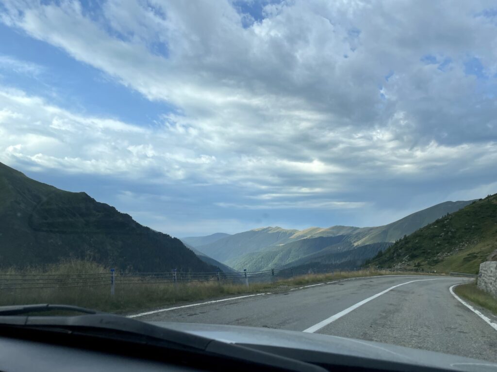 Mountain valley road view from vehicle dashboard, with forested slopes, winding highway, and cloudy sky