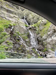 Waterfall cascading down moss-covered rocky cliff face, viewed through a vehicle window