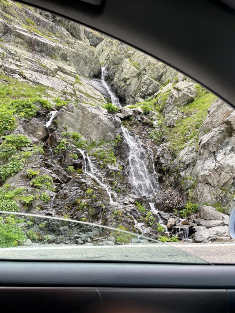Waterfall cascading down moss-covered rocky cliff face, viewed through a vehicle window