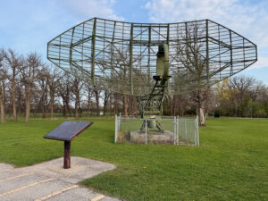 Air Force Heritage Air Park, Winnipeg: Planes, History and Coffee 78 Large green metal radar dish structure mounted on a concrete base with fenced enclosure, displayed in a park setting with interpretive plaque in foreground