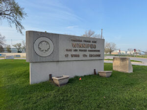 Air Force Heritage Air Park, Winnipeg: Planes, History and Coffee 12 Monument sign for Canadian Forces Base Winnipeg, 17 Wing, with a maple leaf emblem, located on a grass field with buildings and bare trees in the background