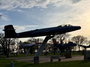 Air Force Heritage Air Park, Winnipeg: Planes, History and Coffee 30 Historic Canadian military aircraft on display in a park, including a dark blue jet fighter mounted on a support structure and a smaller aircraft with red markings visible beneath it