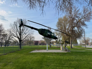 Air Force Heritage Air Park, Winnipeg: Planes, History and Coffee 66 Green military helicopter mounted on a white pedestal in a public park, surrounded by bare and budding trees, with a paved walkway and grassy field