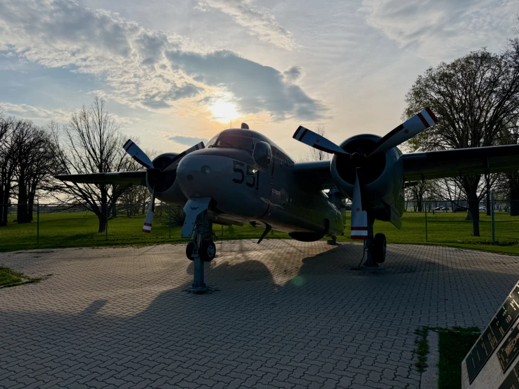 Vintage twin-engine aircraft with number 51 on fuselage, displayed on brick platform in park setting with bare trees and cloudy sky
