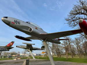 Air Force Heritage Air Park, Winnipeg: Planes, History and Coffee 47 Historic military aircraft on display in a park, including a grey jet marked 186 with red propeller and tail fin, alongside other vintage aircraft and bare trees