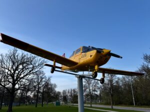 Air Force Heritage Air Park, Winnipeg: Planes, History and Coffee 72 Yellow and black aircraft numbered 228 mounted on a pole in a park, with bare trees and clear blue sky in the background