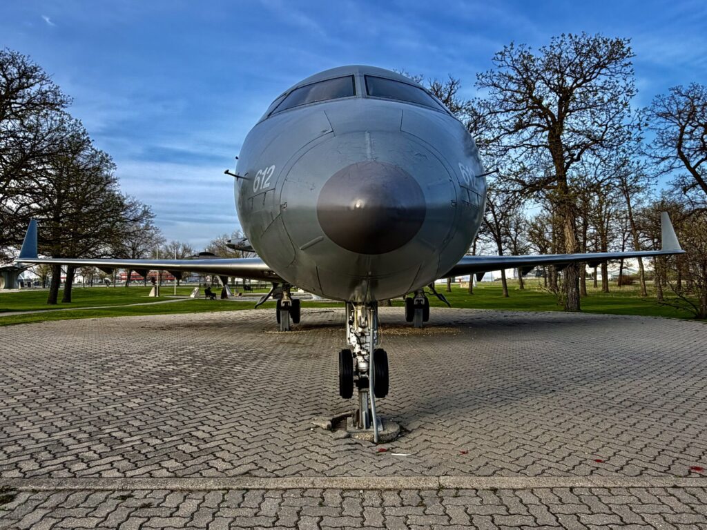 Large commercial aircraft displayed on a paved ground in a park setting, viewed from directly behind showing the fuselage, tail wings, and landing gear
