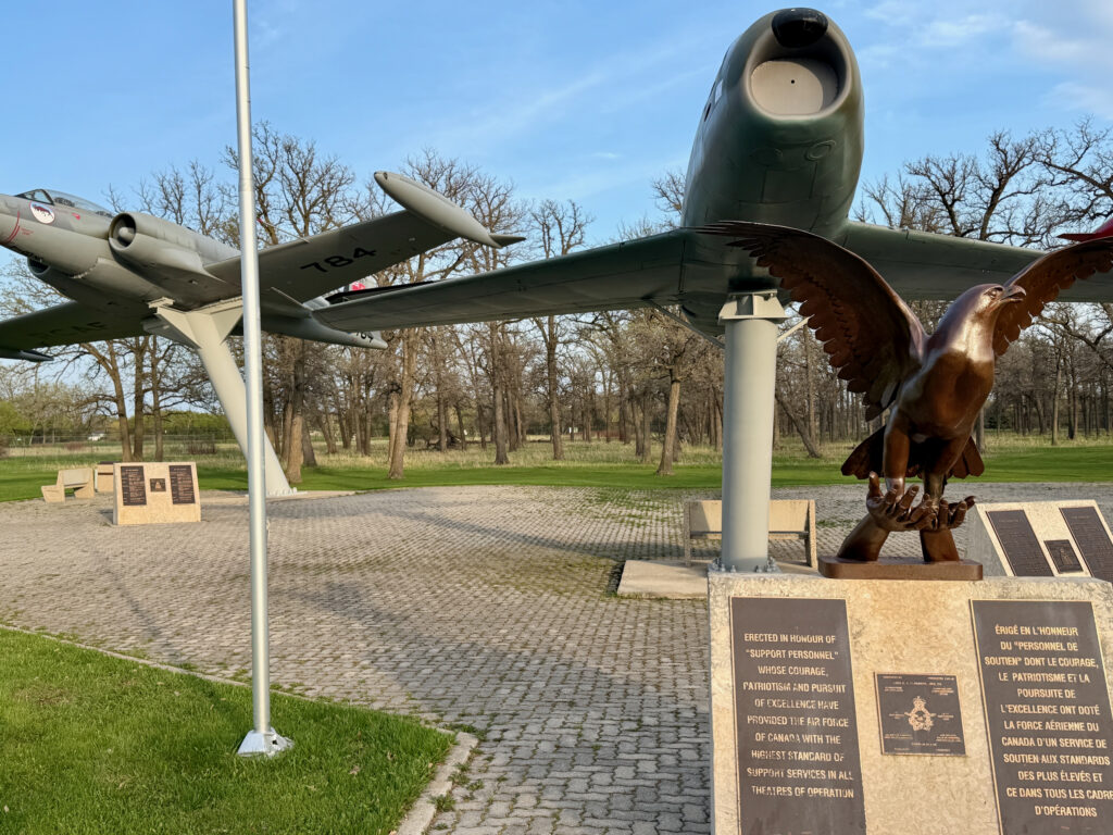 Air Force Heritage Air Park, Winnipeg: Planes, History and Coffee 39 Vintage military aircraft mounted on a pedestal in a memorial park, with a bronze eagle sculpture and bilingual commemorative plaques honouring Canadian Air Force support personnel