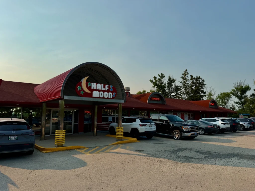 Half Moon restaurant exterior with red metal building, arched entrance, yellow bollards, and parked vehicles in the lot
