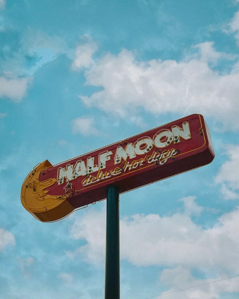 Vintage Half Moon Deluxe Drive-In sign against a blue sky with white clouds