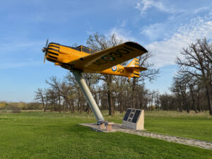 Air Force Heritage Air Park, Winnipeg: Planes, History and Coffee 60 Yellow and black vintage aircraft mounted on a pedestal in a grassy field with bare trees, featuring registration number NC001 and a Canadian military roundel on the fuselage
