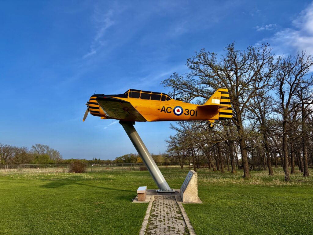 Yellow and black vintage military training aircraft mounted on a pedestal in a park setting, marked with Canadian Air Force roundel and identification number AC301