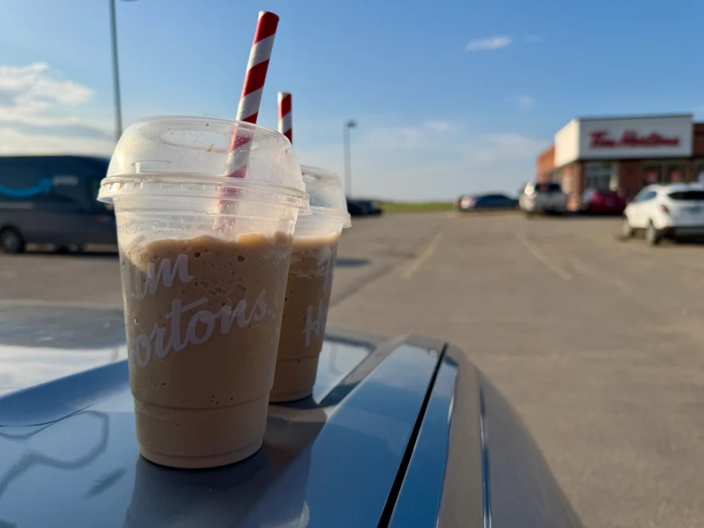 Tim Hortons iced coffee drinks with red and white striped straws on a car hood in a parking lot