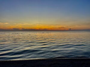 Calm Manitoba lake at sunset with golden and orange sky reflecting on the water, dark pebbled beach in foreground