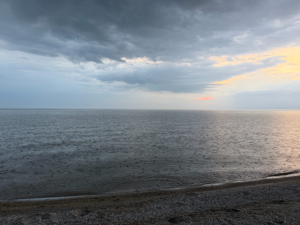 Calm beach at dusk with grey clouds overhead and golden light on the horizon