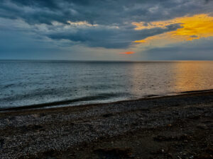 Pebble beach at sunset with stormy clouds breaking to golden light over calm water