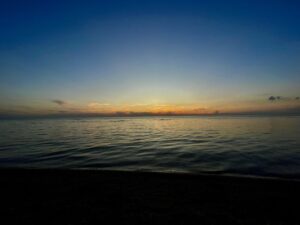 Sunset over calm Manitoba lake waters with golden and orange hues reflecting on the sea, viewed from a dark beach shoreline