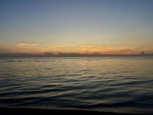 Sunset over calm Manitoba lake waters with golden and orange light reflecting on the surface, clear sky above the horizon