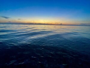 Calm Manitoba lake at sunset with golden light reflecting on the water and a clear blue sky above the horizon