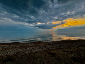 Pebble beach at sunset with dramatic storm clouds and golden light breaking through over calm water