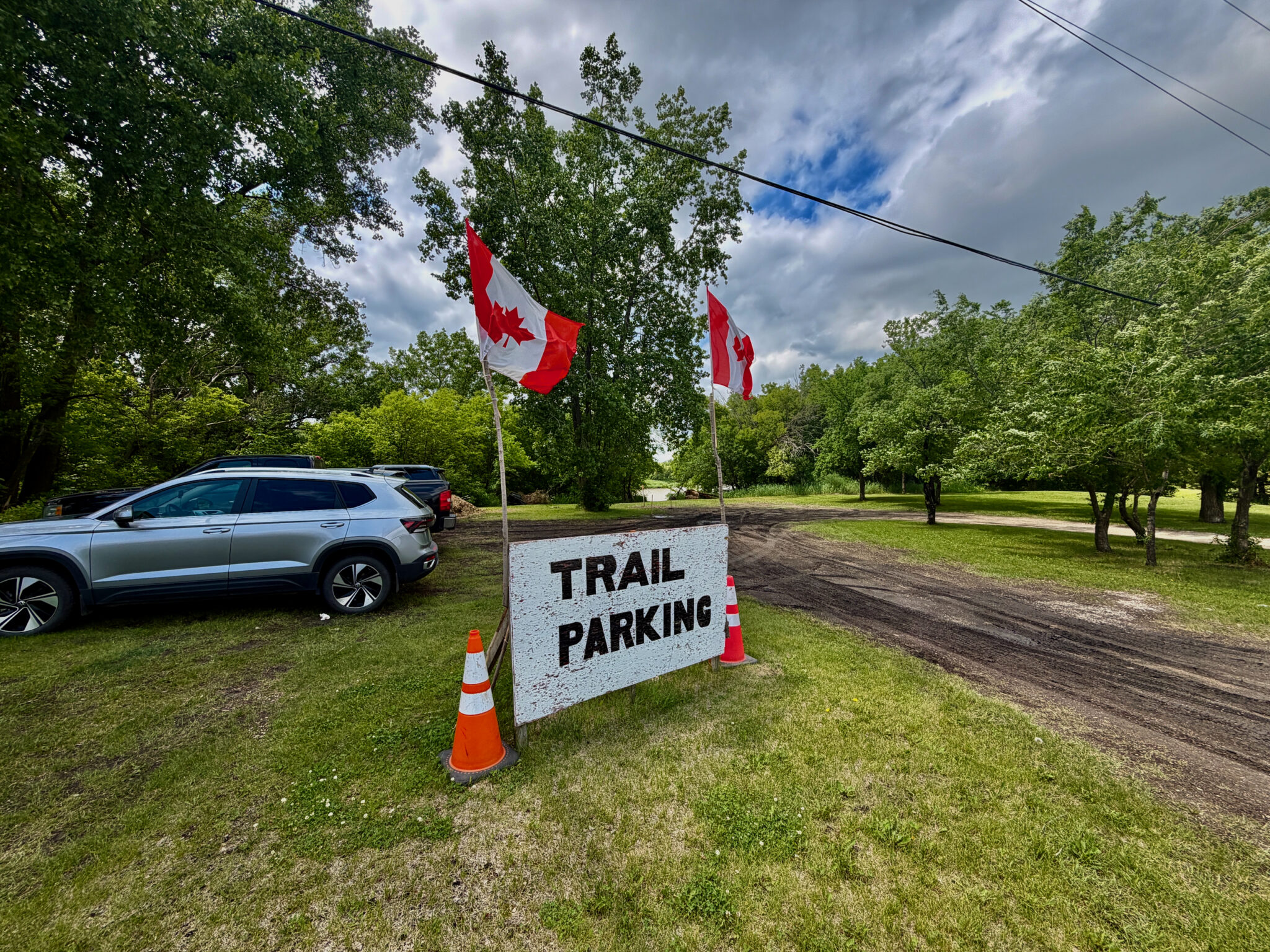 Trail parking area with Canadian flags, parked vehicle, and wooded surroundings