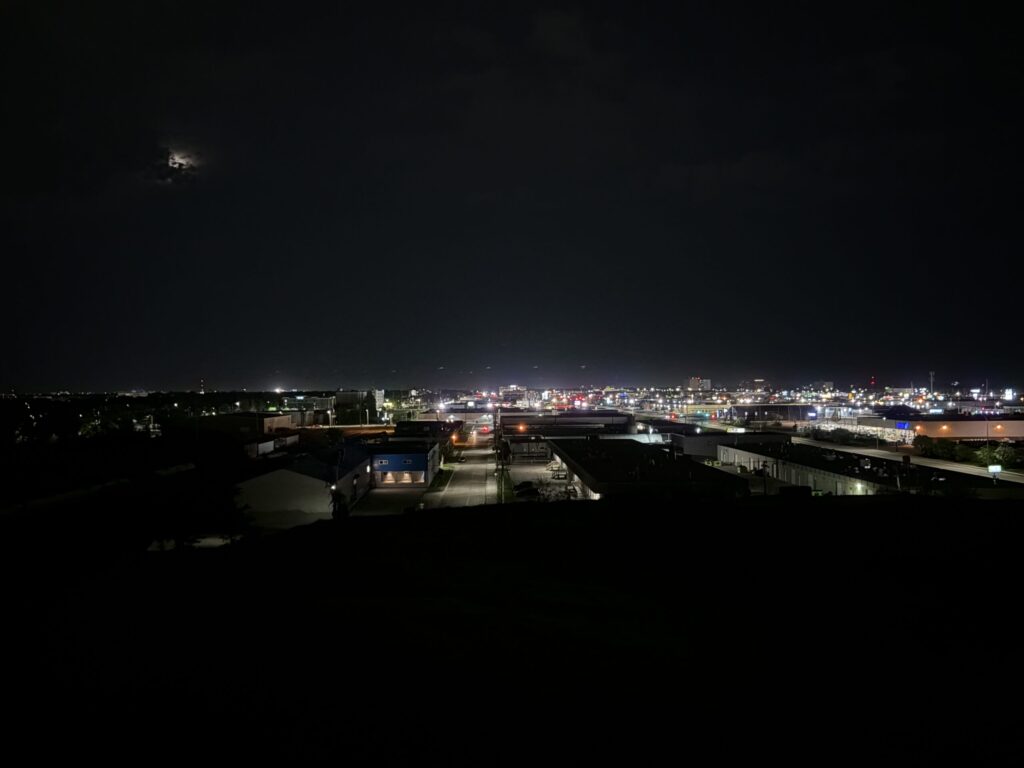 Westview Off-Leash Dog Park: Winnipeg's "Garbage Hill" and the First Park We Ever Walked in Canada 10 A moon peeks through clouds over a city skyline at night, with lights from buildings and streets illuminating the scene