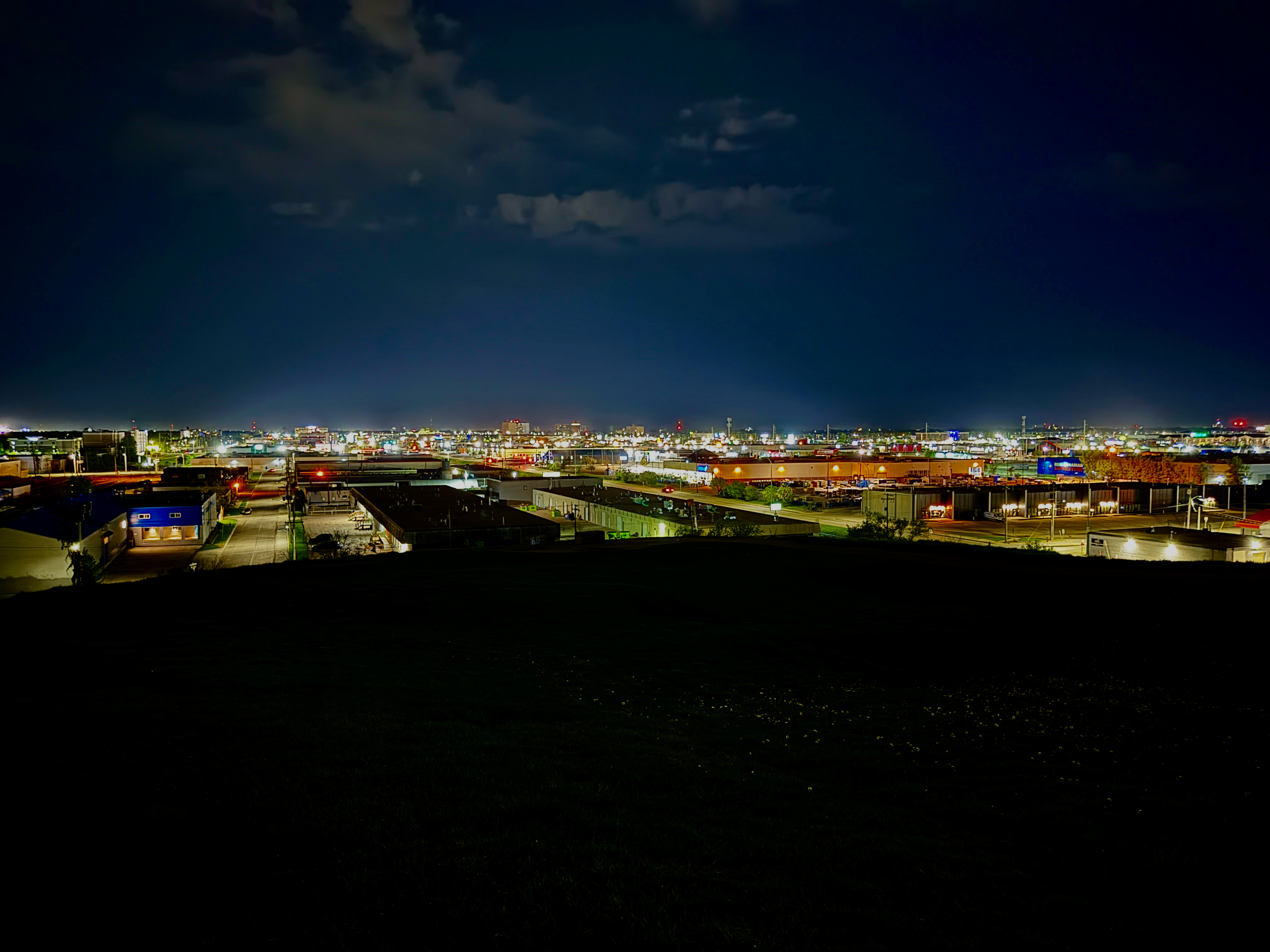 View of an industrial area at night, with lights from buildings and streetlamps illuminating the scene under a cloudy sky