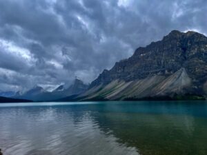 Turquoise alpine lake with dramatic rocky mountains and storm clouds overhead, coniferous forest along the shoreline