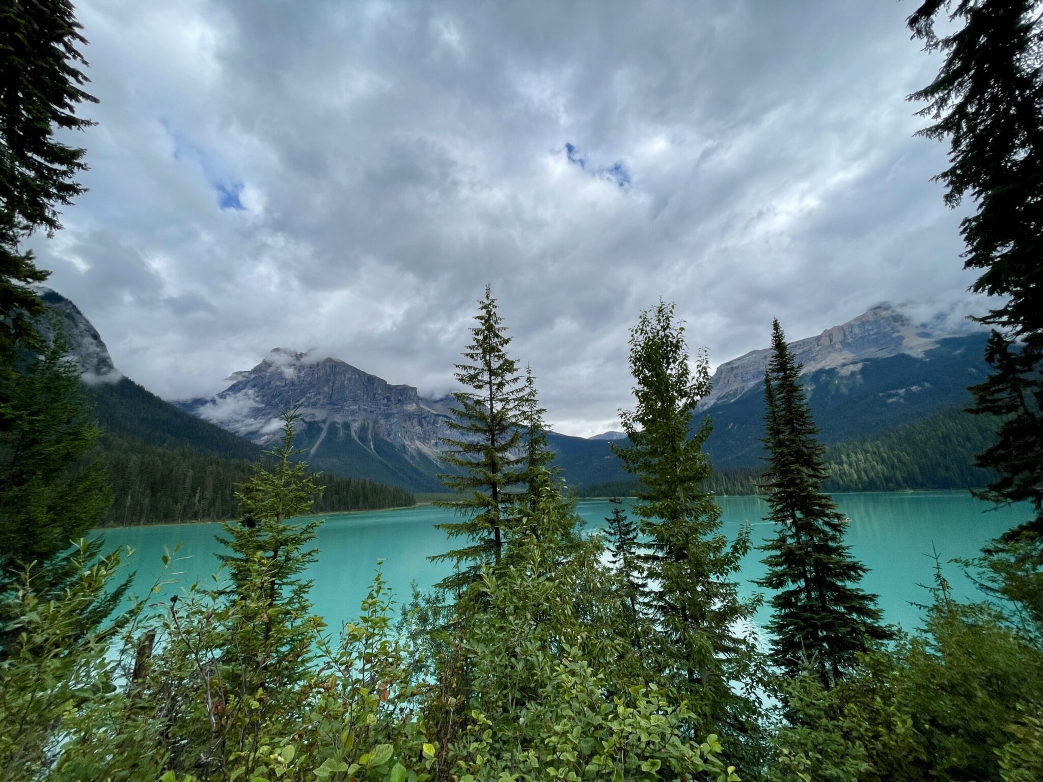 Turquoise alpine lake surrounded by coniferous forest and snow-capped mountains under cloudy sky