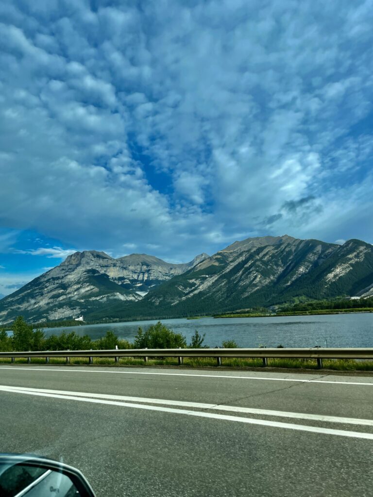 Mountain lake view from highway with forested peaks and dramatic cloudy sky