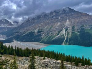 Turquoise alpine lake surrounded by coniferous forest, with dramatic rocky mountains and waterfalls under cloudy skies