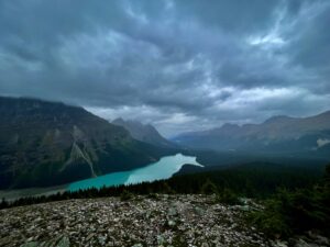 Turquoise glacial lake nestled in a mountain valley surrounded by forested peaks under dramatic cloudy skies