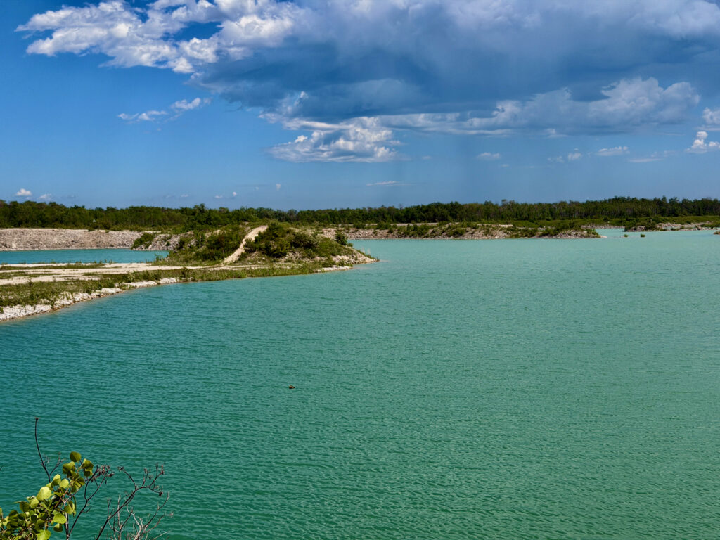 Turquoise lagoon with white limestone shores, dense green forest, and blue sky with white clouds