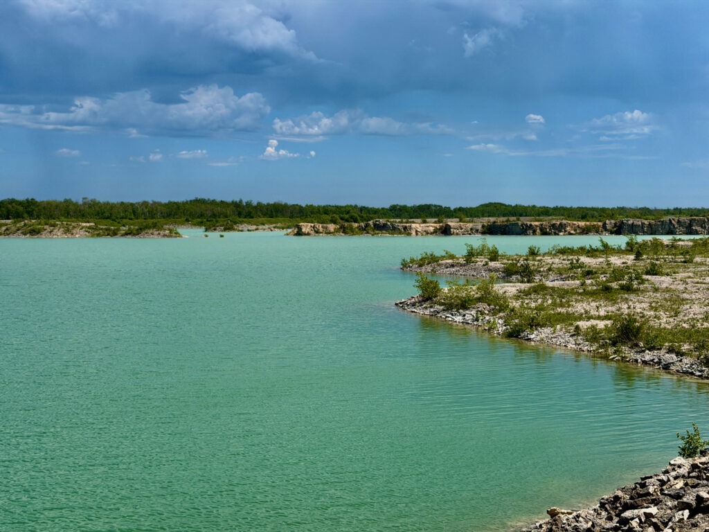 Turquoise water of a quarry lake with rocky limestone shores, forested banks, and blue sky with white clouds