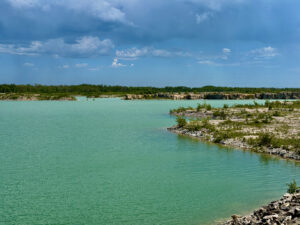 Turquoise water of a quarry lake with rocky limestone shores, forested banks, and blue sky with white clouds