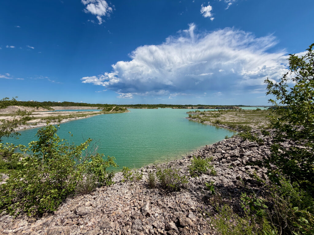 Turquoise lagoon surrounded by rocky limestone shores and mangrove vegetation under a blue sky with white clouds