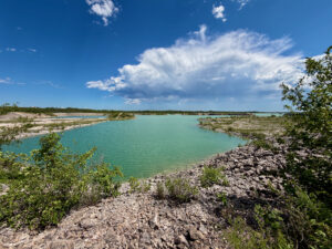Turquoise lagoon surrounded by rocky limestone shores and mangrove vegetation under a blue sky with white clouds