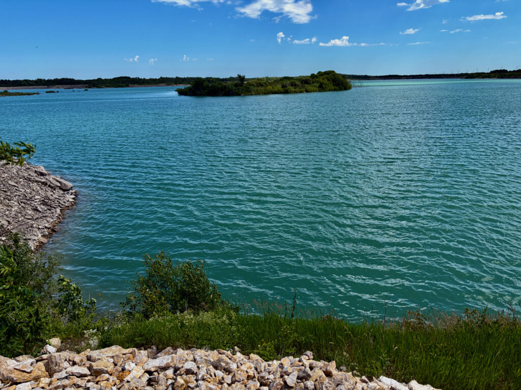 Turquoise lagoon with mangrove islands under clear blue sky, rocky shoreline and coastal vegetation in foreground