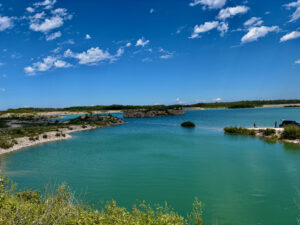 Turquoise lake surrounded by rocky shores, forested banks, and clear blue sky with white clouds